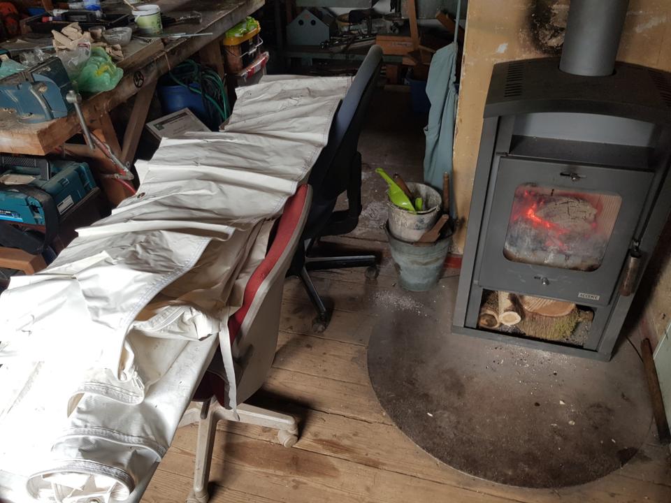 Zeltplane liegt auf Buerostuehlen neben einem Holzofen, um aufzuwaermen.