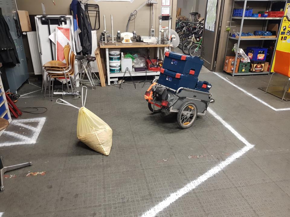 Werkstatt, aufgeraeumt und gefegt, ein Sack mit Spaenen und Fahrradanhaenger mit Werkzeugkisten.