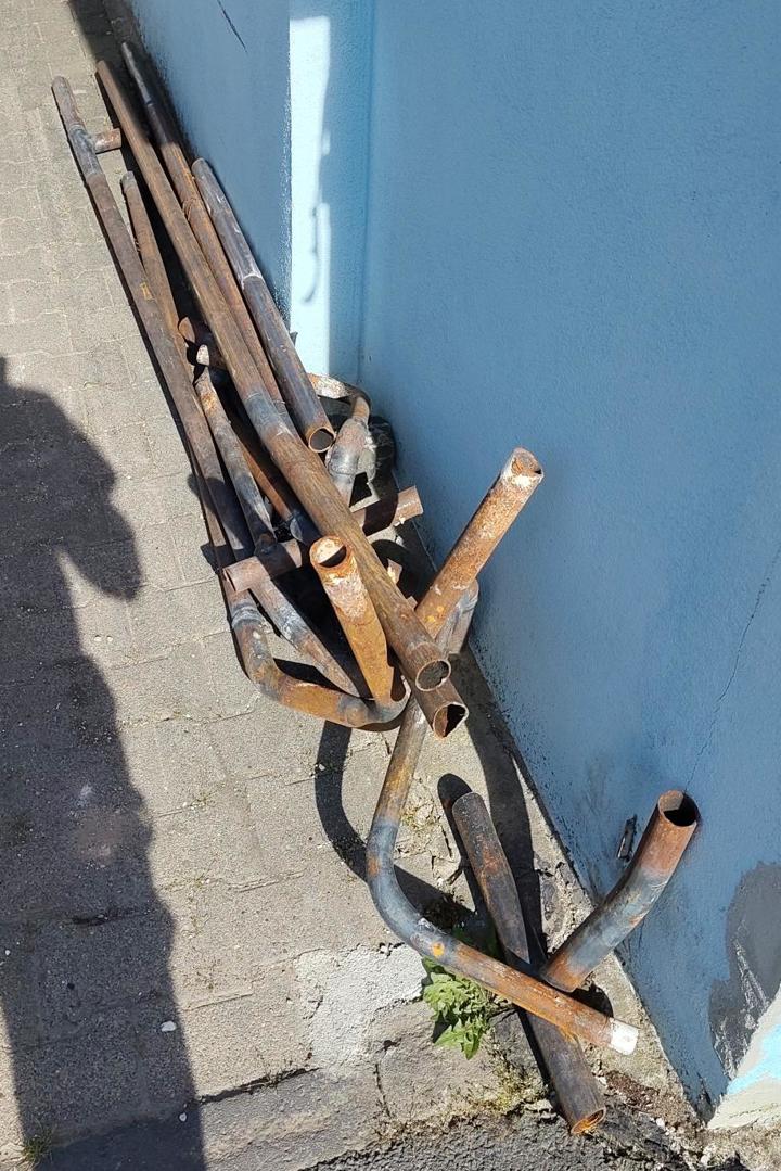 Ein Haufen alter Rohre liegt an einer Hauswand zum Mitnehmen bereit.